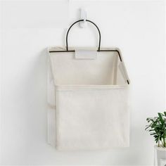 a white hanging bag on the wall next to a potted plant