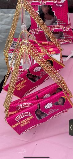 a pink table topped with lots of boxes filled with candy and gold chain necklaces