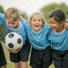 three girls and one boy are holding a soccer ball in front of their faces while smiling