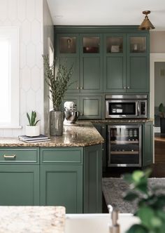 a kitchen with green cabinetry and marble counter tops is pictured in this image, there are plants on the island