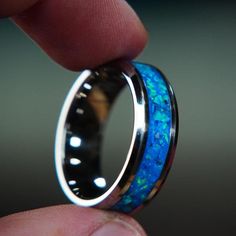 The Winter's Howl is housed in a Tungsten-Carbide ring blank, featuring tanzanite and blue opal. A unique faceted pattern is applied to these tungsten rings to create a truly one-of-a-kind ring. Check out my YouTube video on how I make it: https://www.youtube.com/watch?v=iiFIfKikJRM&t=1s ■ Ring Details - Metal Type: Tungsten-Carbide - Width: 6mm, 8mm - Inlay Materials: tanzanite, blue opal, blue daytime, blue glow - Band: Comfort Fit ■ Resizing: If your ring doesn't fit perfectly, we will be Tungsten Carbide Promise Ring, Round Tungsten Carbide Promise Ring Jewelry, Round Tungsten Carbide Jewelry Gift, Anniversary Rings In Tungsten Carbide, Anniversary Tungsten Carbide Rings, Silver Tungsten Carbide Promise Ring, Silver Tungsten Carbide Ring As Gift, Engagement Ring Opal, Mens Engagement Ring