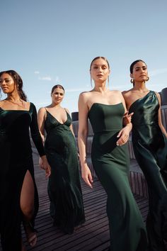 three women in green dresses walking on a wooden deck with one woman looking at the camera