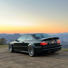 a black car parked on top of a dirt field next to a mountain at sunset