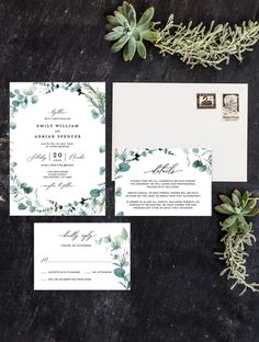 the wedding stationery is set on top of a black surface with greenery around it