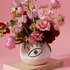 a vase filled with pink and red flowers on top of a wooden block in front of a pink background