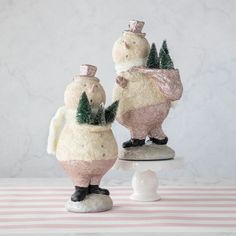 two snowmen with hats and scarfs on top of a cake stand in front of a marble wall