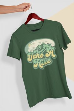 "Introducing our \"Take A Hike\" t-shirt, perfect for outdoor enthusiasts and nature lovers! This comfy and stylish t-shirt features a bold and vibrant graphic of a hiker in action, surrounded by scenic mountain vistas. Made from soft and breathable cotton material, this tee is perfect for wearing on your next hiking trip, or for simply showing your love for the great outdoors. The \"Take A Hike\" message emblazoned on the shirt serves as a reminder to take a break from the hustle and bustle of Outdoor Crew Neck T-shirt With Letter Print, Green Graphic Tee For Outdoor, Green Graphic Print T-shirt For Camping, Graphic Tee With Text Print For Camping, Pre-shrunk Green T-shirt For Camping, Green Short Sleeve T-shirt For Outdoor, Crew Neck T-shirt With Letter Print For Hiking, Green Graphic Tee For Outdoor Activities, Green T-shirt For Outdoor Activities