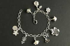 A collection of silver plated flower charms, combined with a trio of handmade flower charms designed from glass pearls in your choice of color and silver plated petals, have been dispersed around a shimmering silver plated bracelet chain in this handmade charm bracelet. This flower charm bracelet is then completed with a lobster clasp and a 1/2 inch of chain at the end for adjustable sizing. Please see the last picture in this listing for a sample view of all pearl colors available for this brac Silver Metal Charm Bracelet With Pearl Charm, Elegant Handmade Flower Charm Bracelet, Elegant Flower Charm Bracelet For Jewelry Making, Silver Jewelry With Flower Charm, Charming Silver Jewelry With Flower Charm, Silver Flower Jewelry With Pearl Charm, Silver Floral Jewelry With Pearl Charm, Silver Flower-shaped Jewelry With Pearl Charm, Dog Charm Bracelet