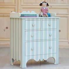 a doll sitting on top of a blue and white striped dresser with books in it's drawer