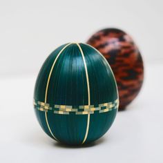 two green and gold decorated eggs sitting next to each other on a white table top