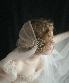 a woman wearing a white dress with a veil on her head and flowers in her hair