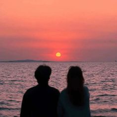 two people sitting on the beach watching the sun set