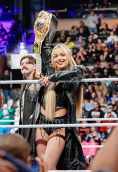 a woman holding up a trophy in the middle of a wrestling ring with other people watching