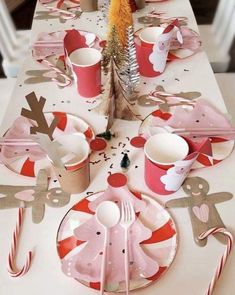 the table is set with pink and white plates, cups, spoons and forks