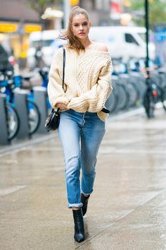 a woman walking down the street wearing jeans and a sweater