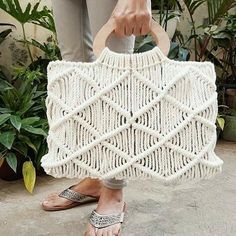 a woman holding a white crocheted bag in her hands and sandals on the ground