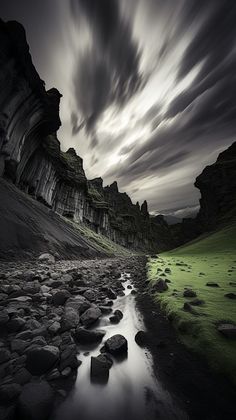 a river running through a lush green valley under a cloudy sky with rocks and grass