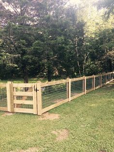 a wooden fence in the middle of a grassy area with trees and bushes behind it