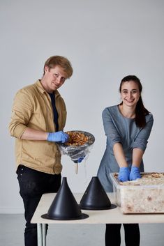 two people standing next to each other near a table with food on top of it