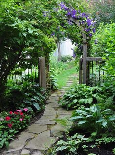 a garden with lots of green plants and flowers on the path to an open gate