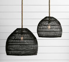 two black rattan lamps hanging from rope against white wall with horizontal lines in the background