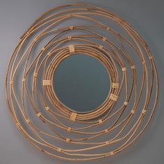 a circular mirror made out of bamboo sticks on top of a gray wall with a reflection in the middle