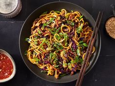 a bowl filled with noodles and vegetables next to chopsticks on a black surface