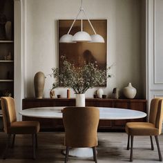 a dining room table with four chairs and a vase on the wall behind it in front of a painting