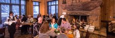 a group of people sitting around a table in front of a fire place filled with food