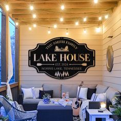 an outdoor living area with furniture and string lights hanging from the ceiling, along with a lake house sign on the wall