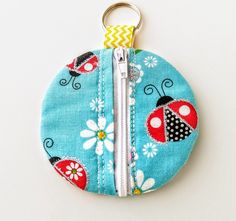 a zippered coin purse with ladybugs and daisies on blue fabric, hanging from a metal hook