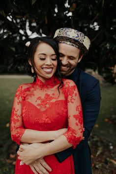 a man and woman hugging each other in front of trees