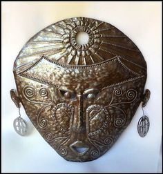 a decorative mask with earrings hanging from it's side on a white wall background