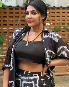 a woman standing in front of a wooden fence wearing a black top and patterned skirt