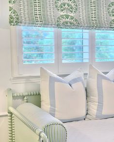 a bed with two pillows on top of it next to a window covered in roman shades