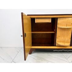 a wooden cabinet with two doors and drawers on the bottom, in front of a white wall