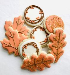 four decorated cookies with frosting and sprinkles in the shape of leaves