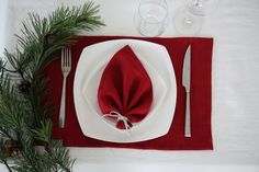 a place setting with red napkins, silverware and pine branches on the table