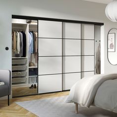 a bedroom with a bed, chair and white wardrobes in it's corner