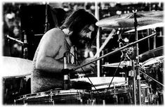 a man with long hair playing drums in front of other drummer's instruments on stage