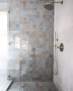 a walk in shower sitting next to a white wall and tiled floor with a hand held shower head