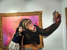 a woman standing next to a giant monkey holding a cell phone in front of a painting