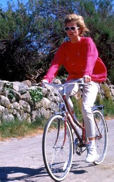 the woman is riding her bike down the road in front of some rocks and trees