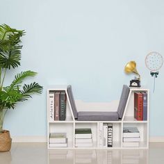 a white book shelf with books and a lamp on top of it next to a potted plant