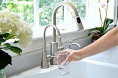 a woman is filling a glass with water from the faucet in her kitchen sink