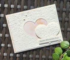 a card with two hearts on it sitting next to some green leaves and a potted plant