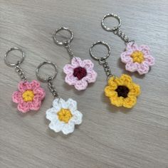 four crocheted flower keychains on a table, one is pink, the other is yellow