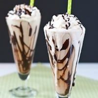 two glasses filled with ice cream and chocolate milkshakes on top of a table