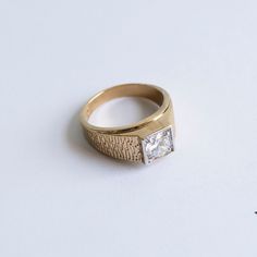 a gold ring with a princess cut diamond on it's side, sitting on a white surface