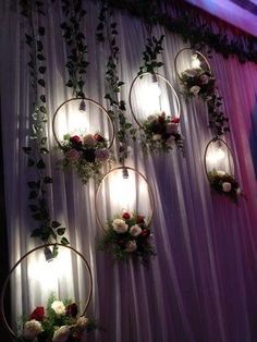 flowers and greenery are hanging on the wall with lights in front of them at a wedding reception